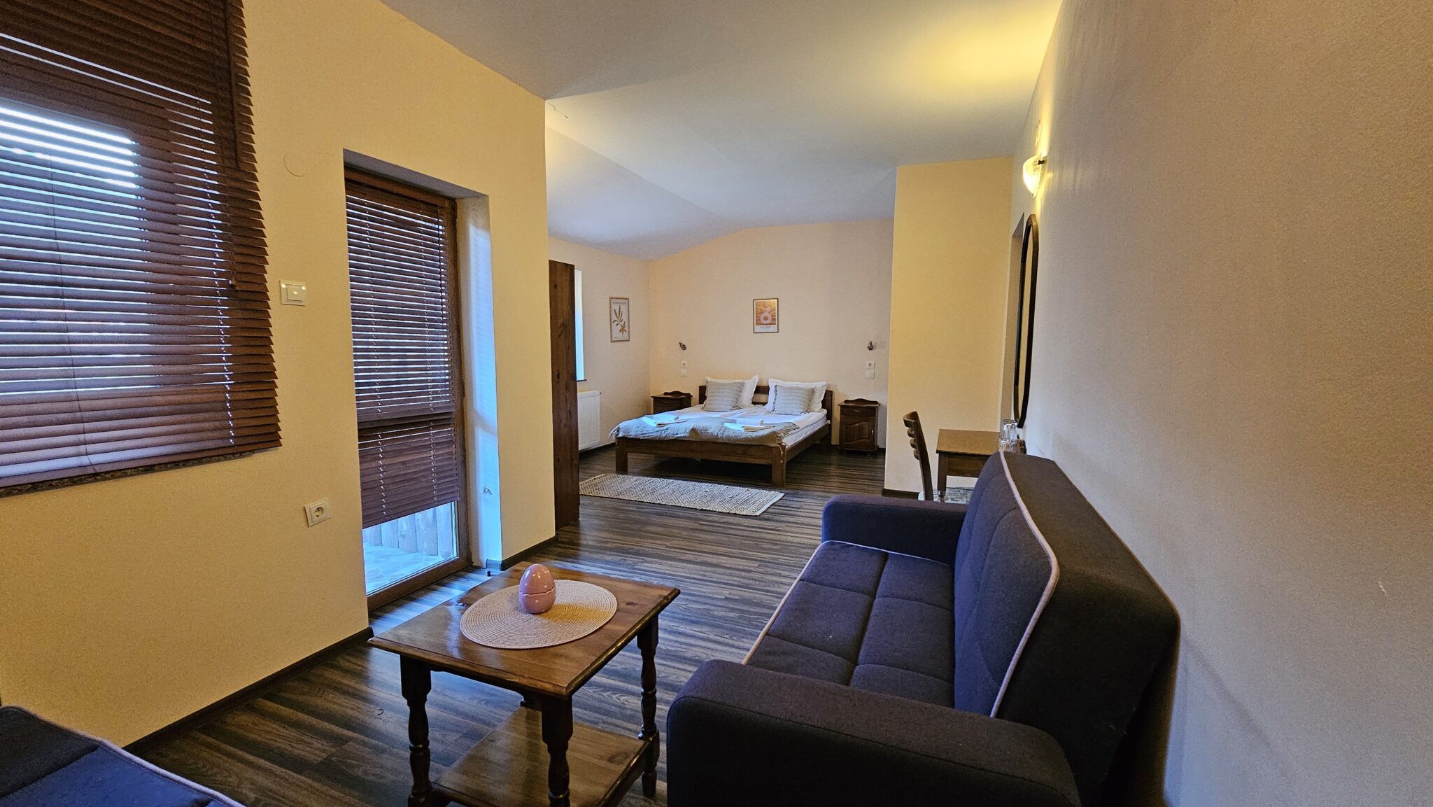 The sofa bed and coffee table, the bed behind, and the balcony door