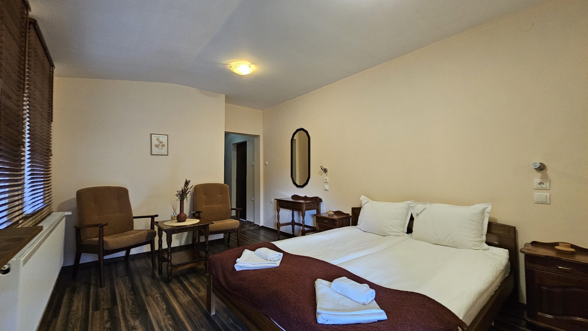Two armchairs with a table, the bed on the right and a mirror on the wall