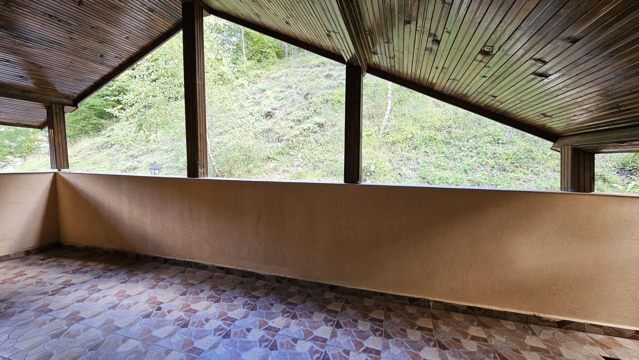 The covered balcony with a wooden ceiling, looking onto the hillside